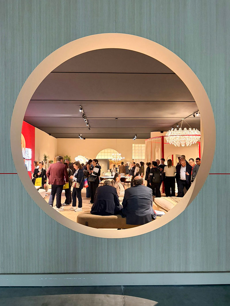 Interior design exhibition seen through a circular window with people exploring a modern showroom space