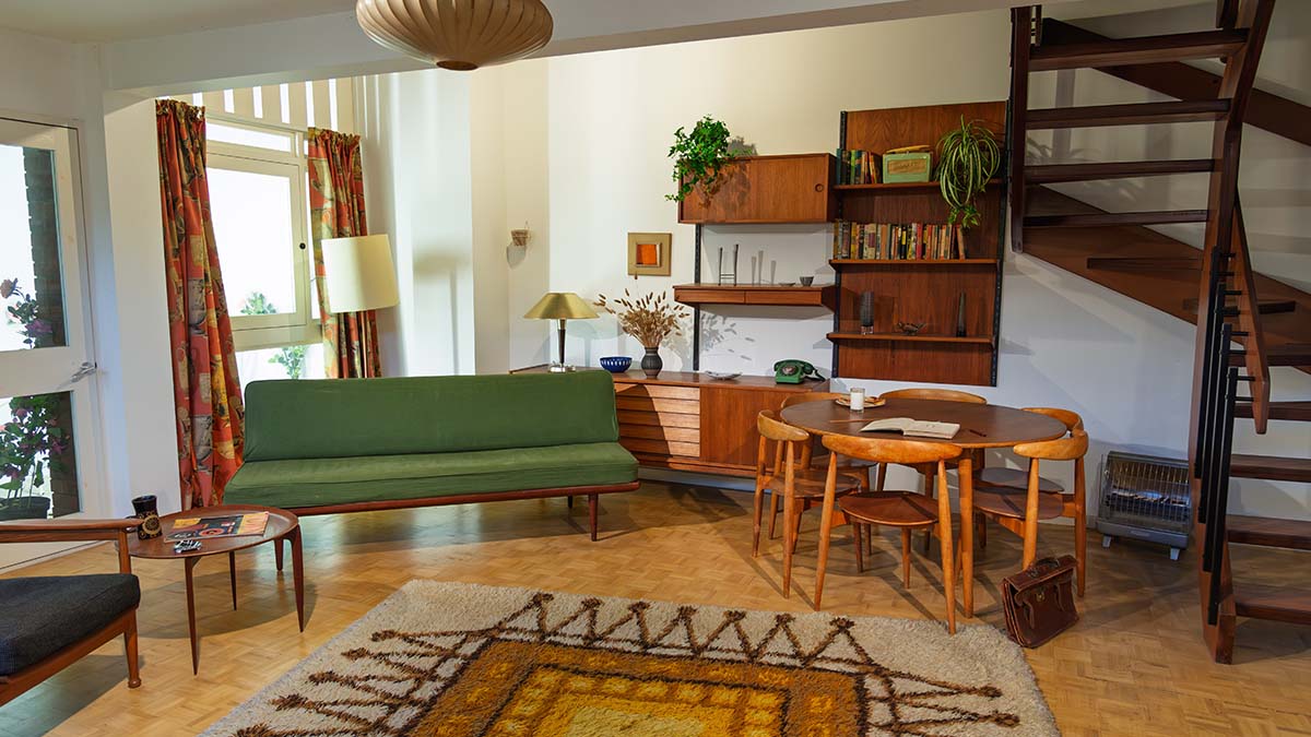 Mid-century modern living room with wooden furniture, green sofa, open staircase and vintage décor