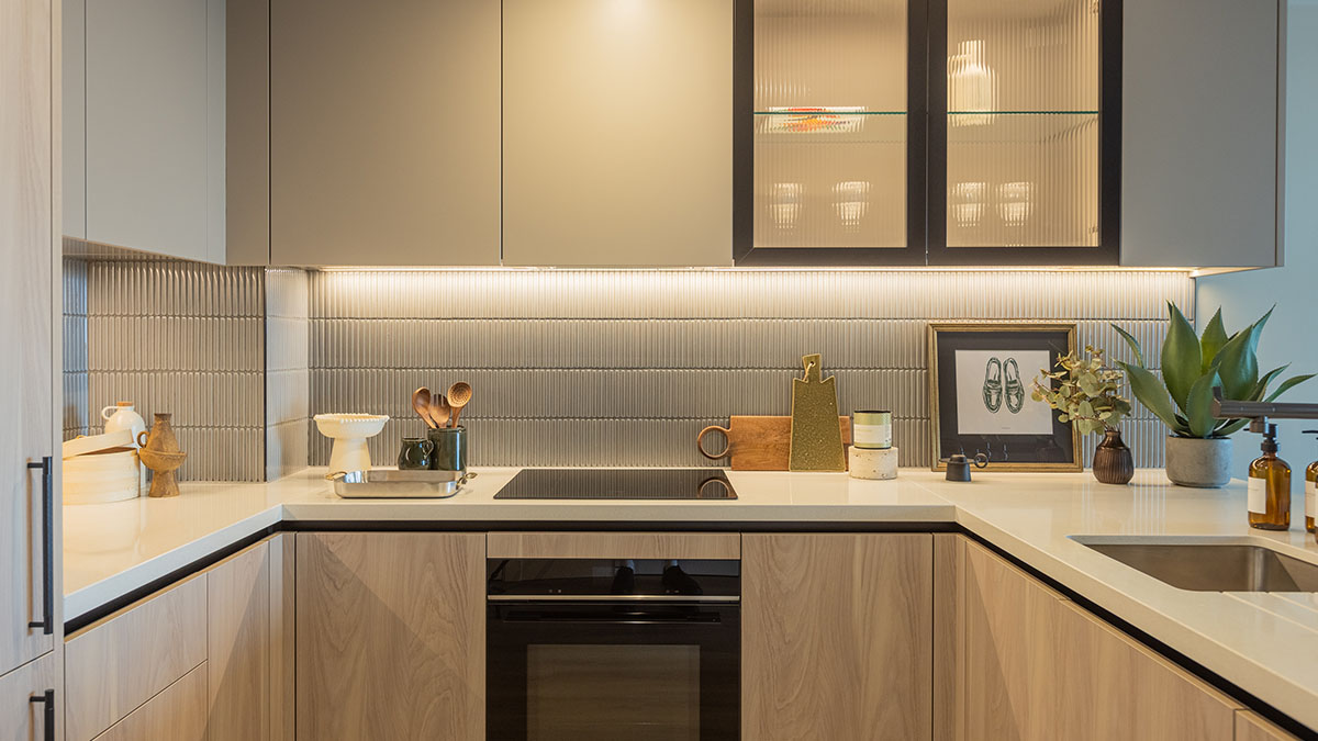 Modern kitchen interior at Regents View featuring wooden cabinetry, textured tiled splashback, integrated appliances, under-cabinet lighting, and styled countertops.