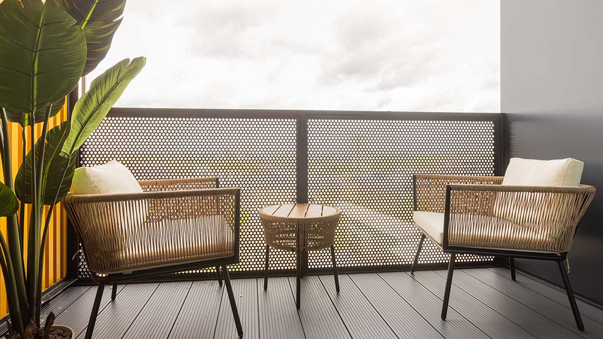 Contemporary balcony seating area at Regents View featuring woven outdoor chairs, a small table, privacy screening, and modern apartment styling.