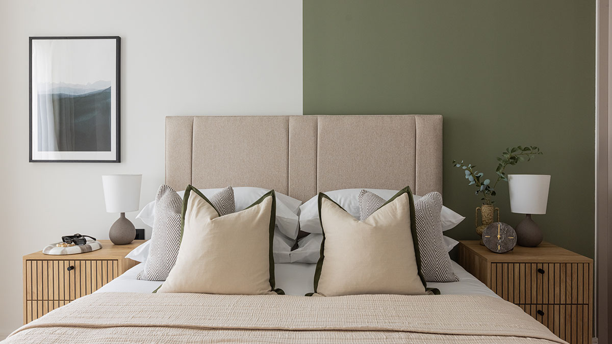 Modern bedroom interior at Regents View featuring a green feature wall, upholstered bed, neutral cushions, wooden bedside tables, and contemporary styling.