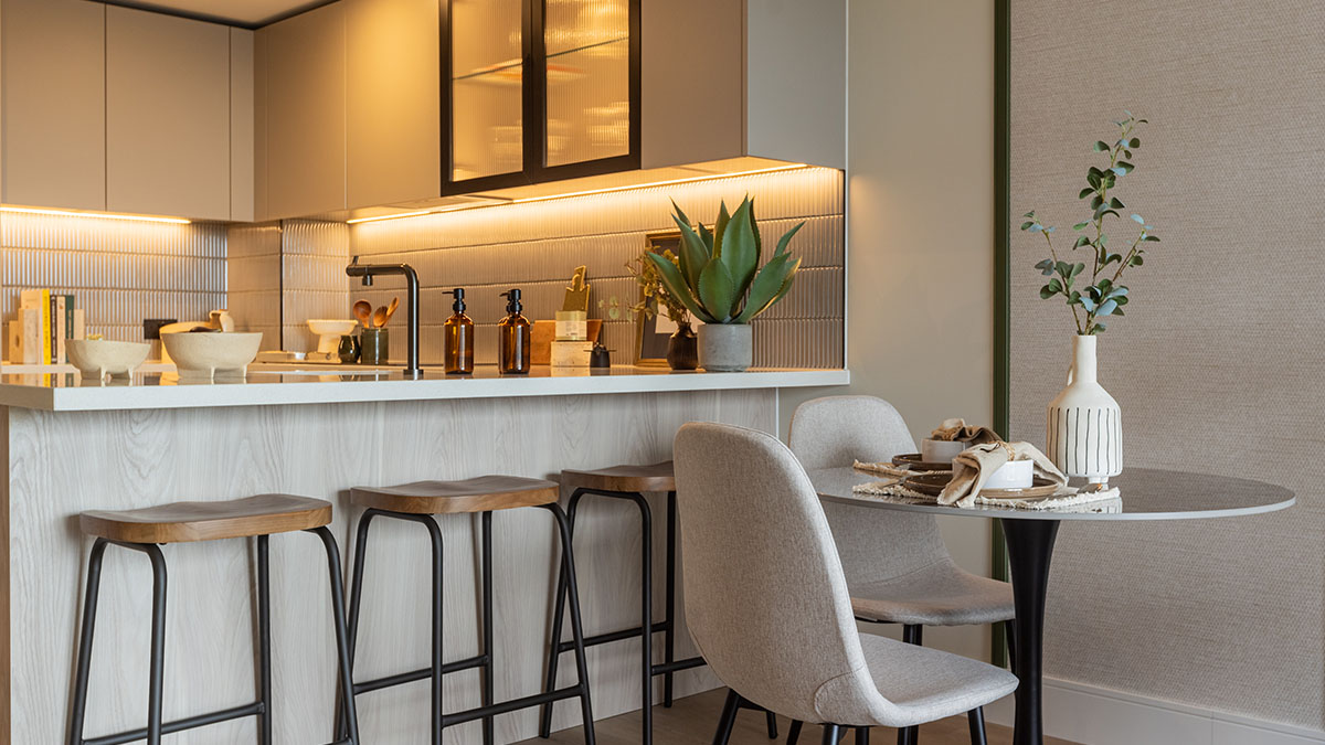 Contemporary kitchen and dining area at Regents View featuring a breakfast bar, wooden stools, textured splashback, warm lighting, and neutral interior styling.