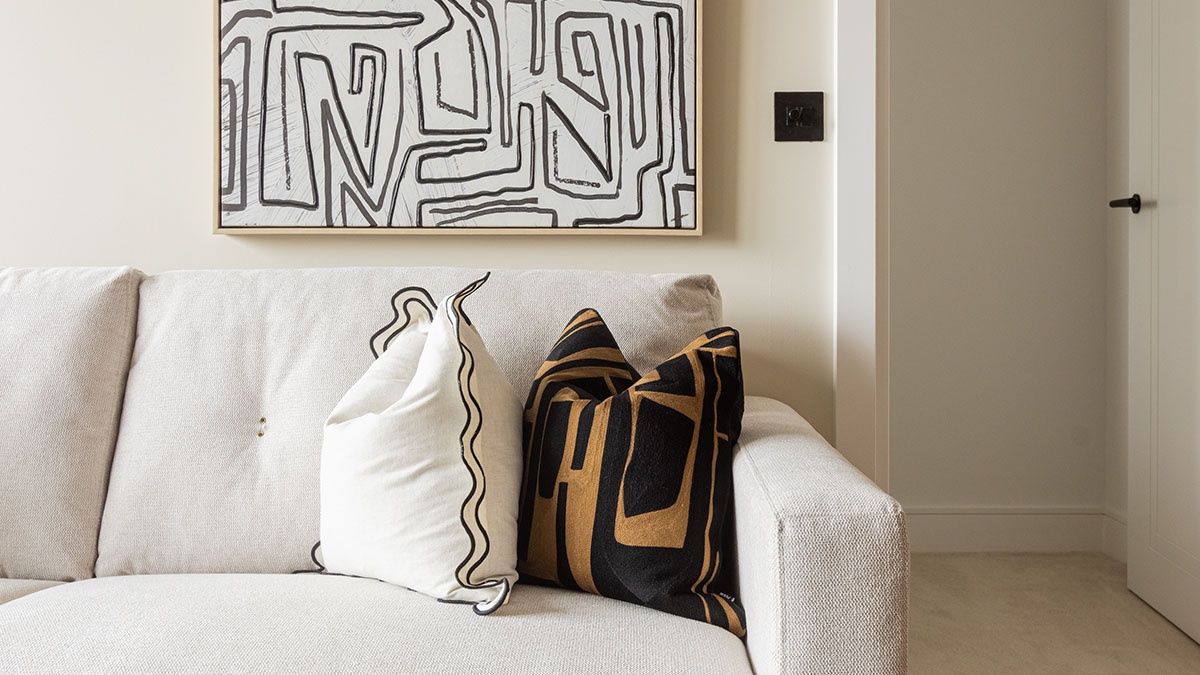 Modern living room featuring a white sofa with decorative cushions and contemporary wall art in a neutral interior setting.