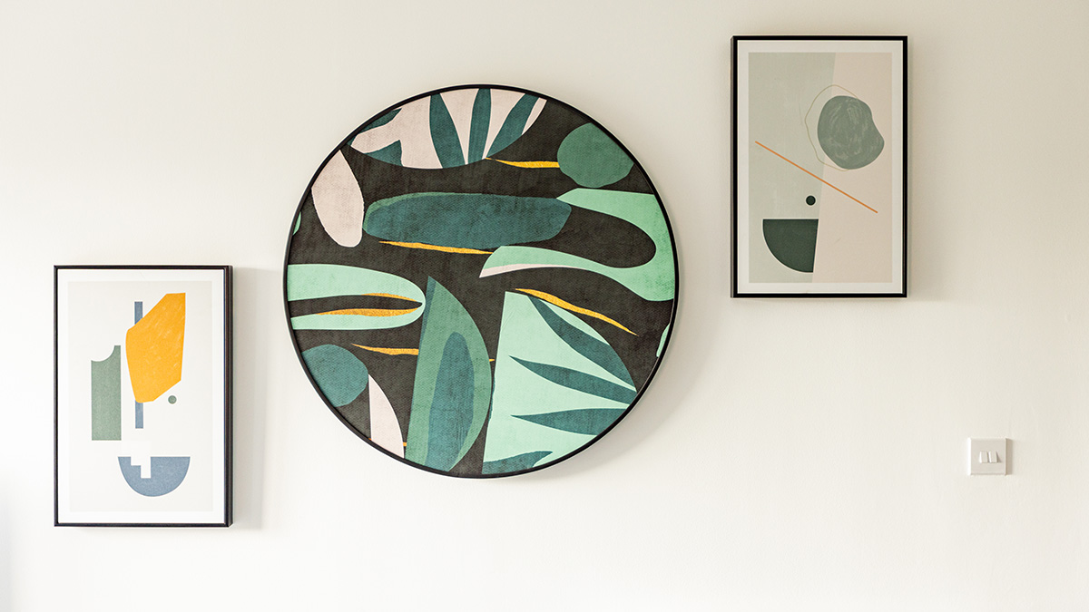 Modern abstract wall art display featuring framed geometric prints and a circular botanical artwork on a minimalist white interior wall.