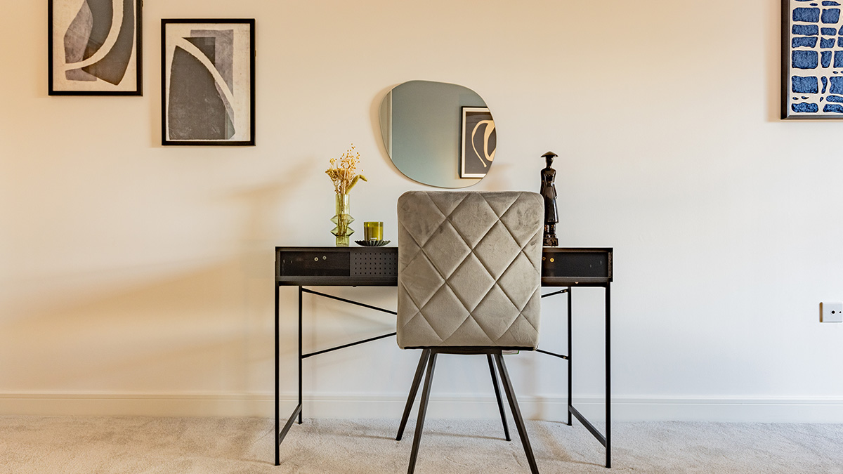 Modern home office corner featuring a black desk, upholstered chair, round mirror, decorative accessories, and abstract wall art in a contemporary interior.