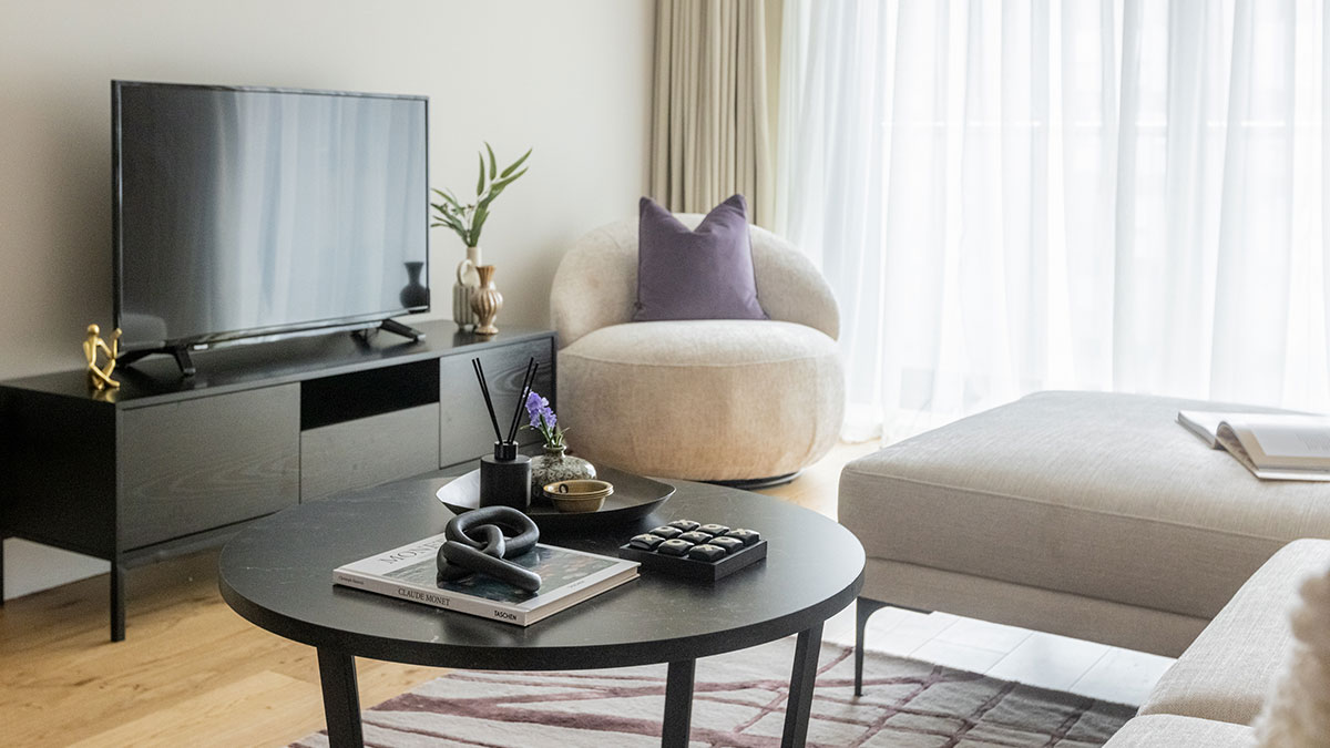 Contemporary living room featuring a black coffee table, TV unit, accent chair and neutral-toned seating.
