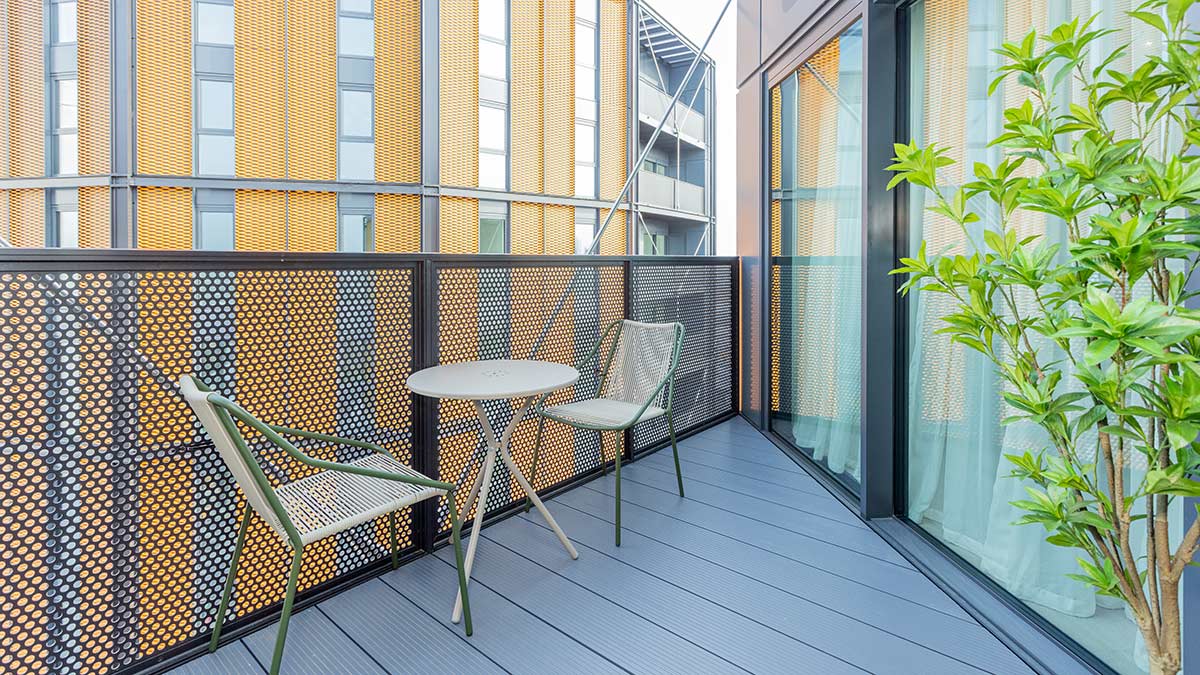 Modern apartment balcony with outdoor table and chairs overlooking contemporary residential buildings.