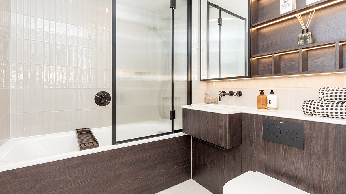 Modern bathroom featuring a bathtub with glass shower screen, dark wood vanity, and illuminated mirror cabinet.