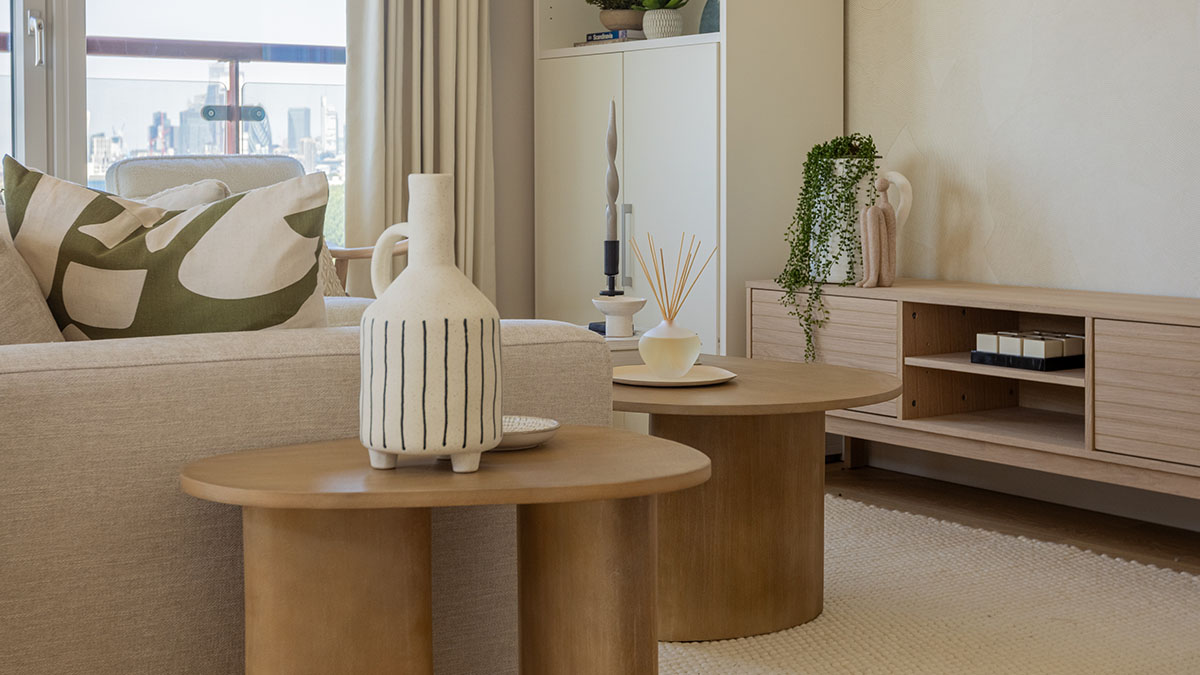 Contemporary living room with neutral furnishings, wooden coffee tables, decorative accessories, built-in storage, and large windows overlooking the city skyline.