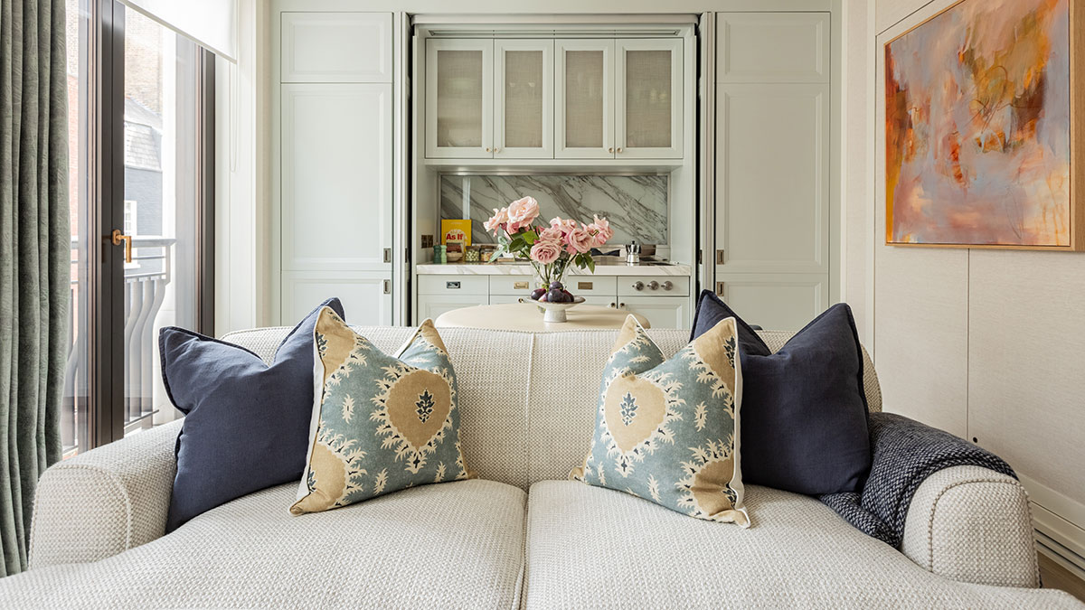 Luxury open-plan living room with a textured sofa, decorative cushions, bespoke kitchen cabinetry and contemporary artwork in a London apartment.