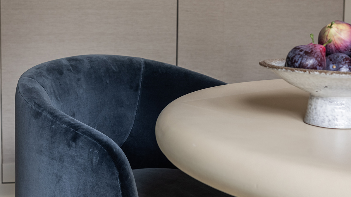 Modern dining area featuring a blue velvet dining chair, round stone-effect table and decorative fruit bowl in a luxury London apartment.