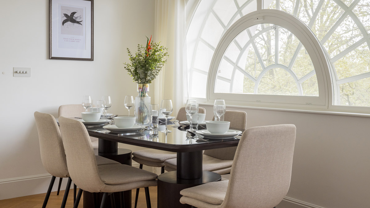 Modern dining room with elegant table setting and large arched feature window in a furnished Millbank SW1P apartment.