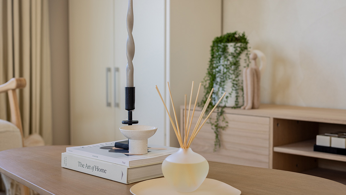 Modern living room coffee table styled with decorative accessories, books, candle holder, reed diffuser, and contemporary shelving in a neutral interior