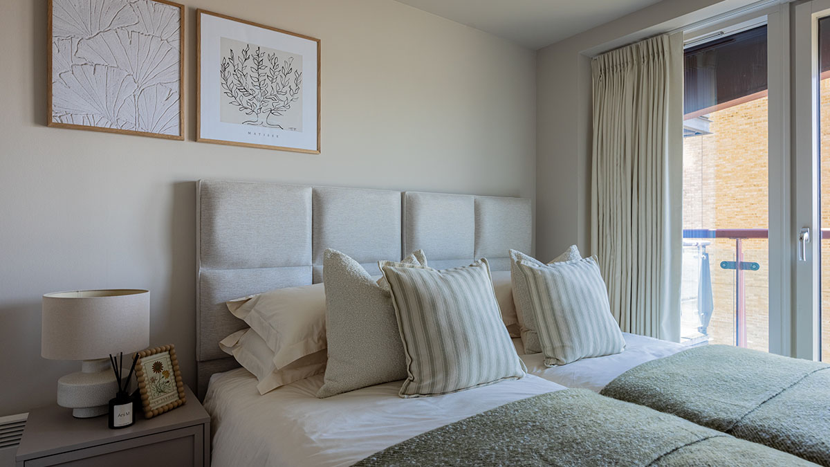 Contemporary bedroom with a padded upholstered headboard, neutral bedding, framed wall art, bedside table, and balcony access.