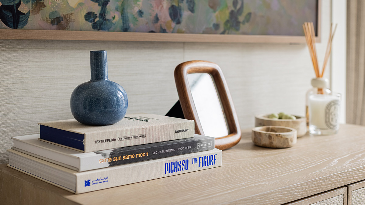Styled console table with decorative books, ceramic vase, framed mirror and reed diffuser in a luxury London apartment interior.