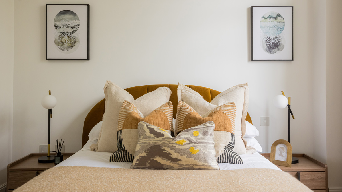 Stylish double bedroom with velvet headboard, decorative cushions and modern bedside lighting in a Millbank London apartment.
