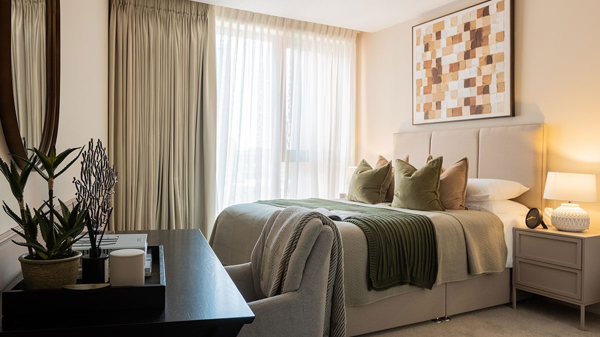 Stylishly furnished bedroom at West End Gate featuring a padded headboard, olive green cushions, bedside lamps and contemporary artwork.