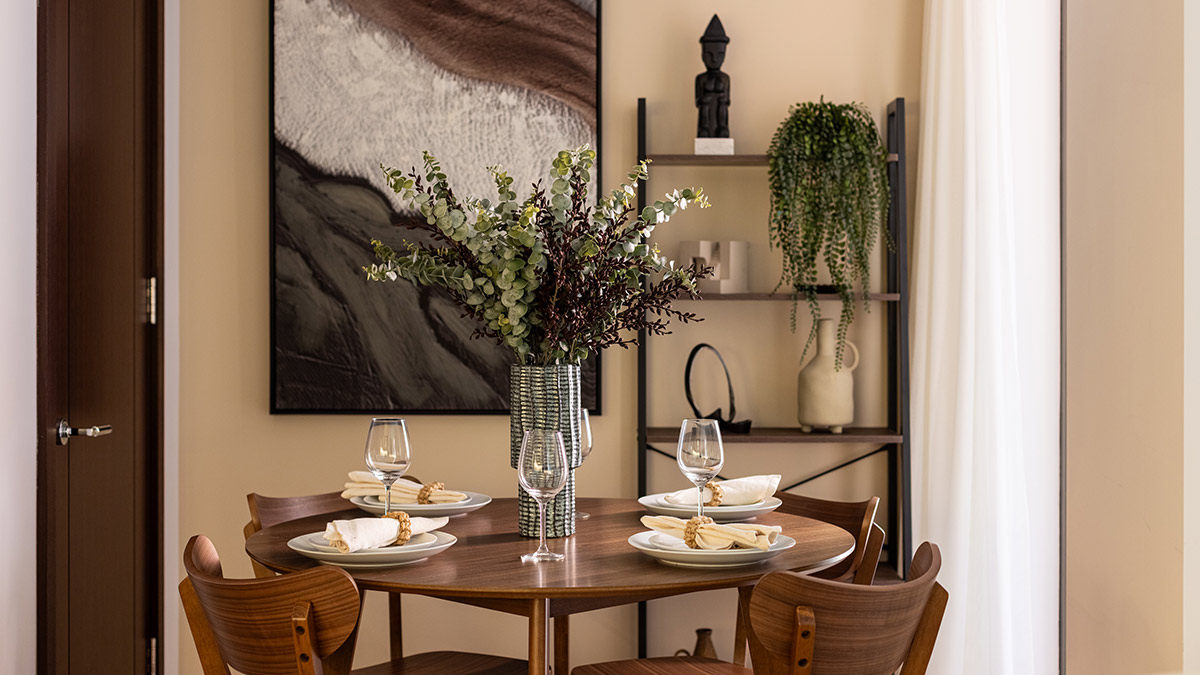 Modern dining area in a West End Gate apartment with a round wooden table, feature artwork and curated decorative shelving.