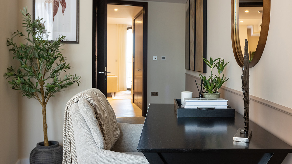 Home office setup with a black desk, upholstered chair, decorative mirror and indoor plants in a furnished West End Gate apartment.
