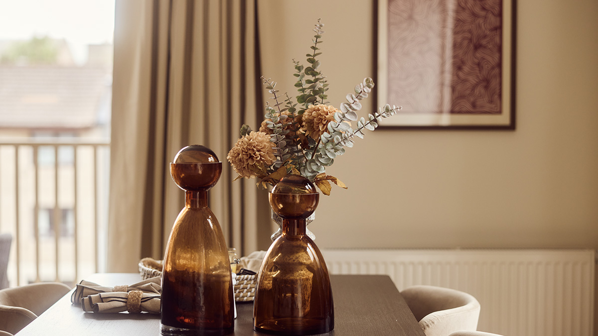 BTR dining area with amber glass vases, dried floral arrangement, dining table and neutral upholstered chairs.