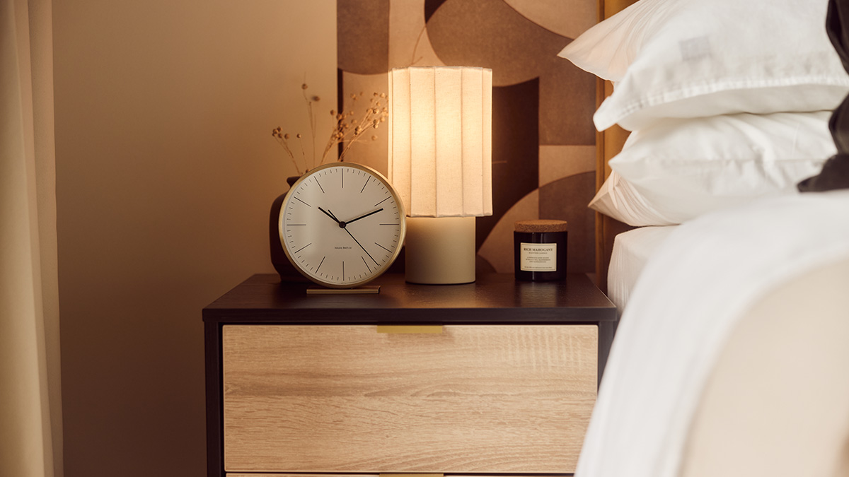 BTR bedroom bedside table with a modern lamp, clock, candle and neutral bedding, creating a warm and inviting interior.