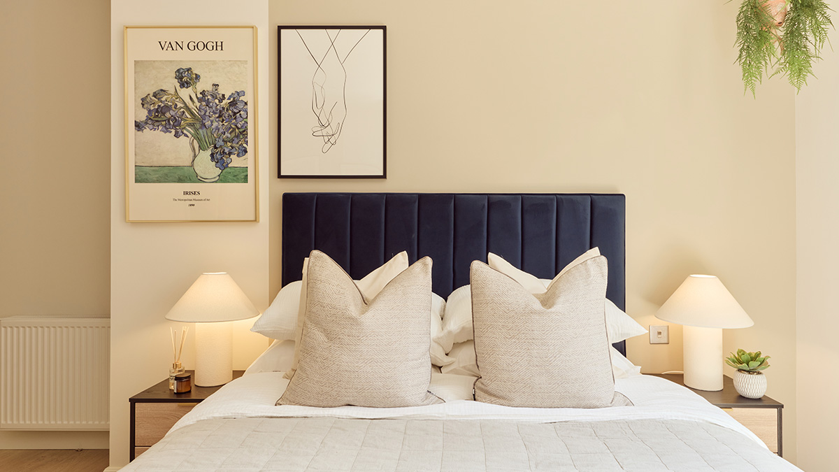 Luxury bedroom featuring a navy upholstered headboard, framed artwork and premium bedding.
