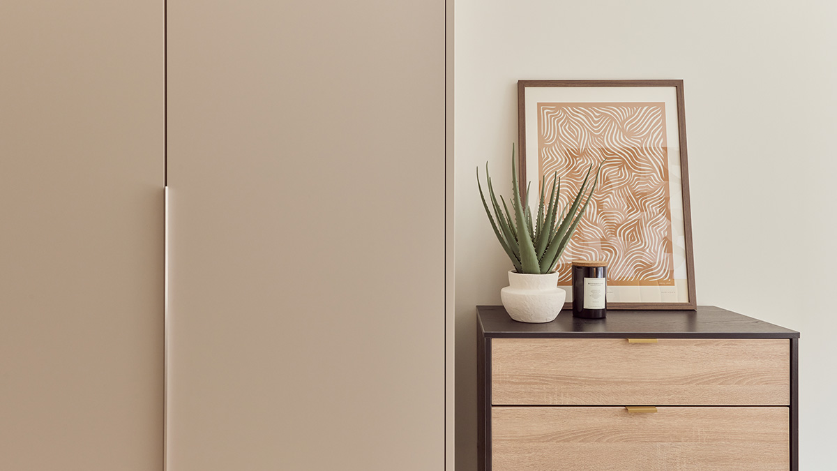Contemporary bedroom storage featuring a wooden chest of drawers, framed artwork, candle and indoor plant.