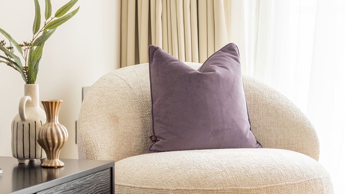 Beige boucle accent chair with purple cushion and decorative vases