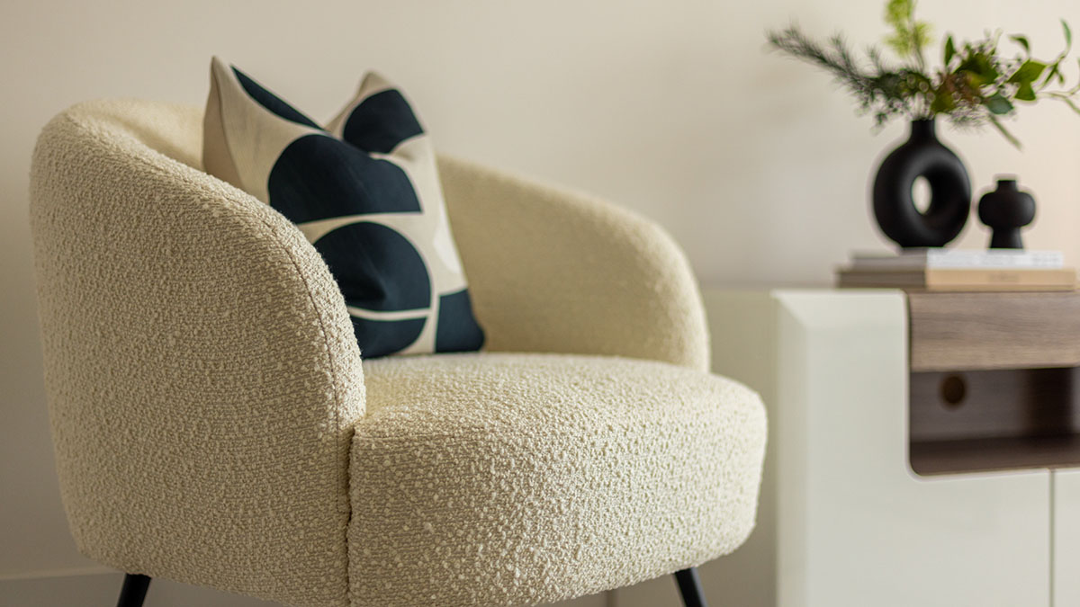Cream boucle armchair with black and white cushion beside a modern wooden side table