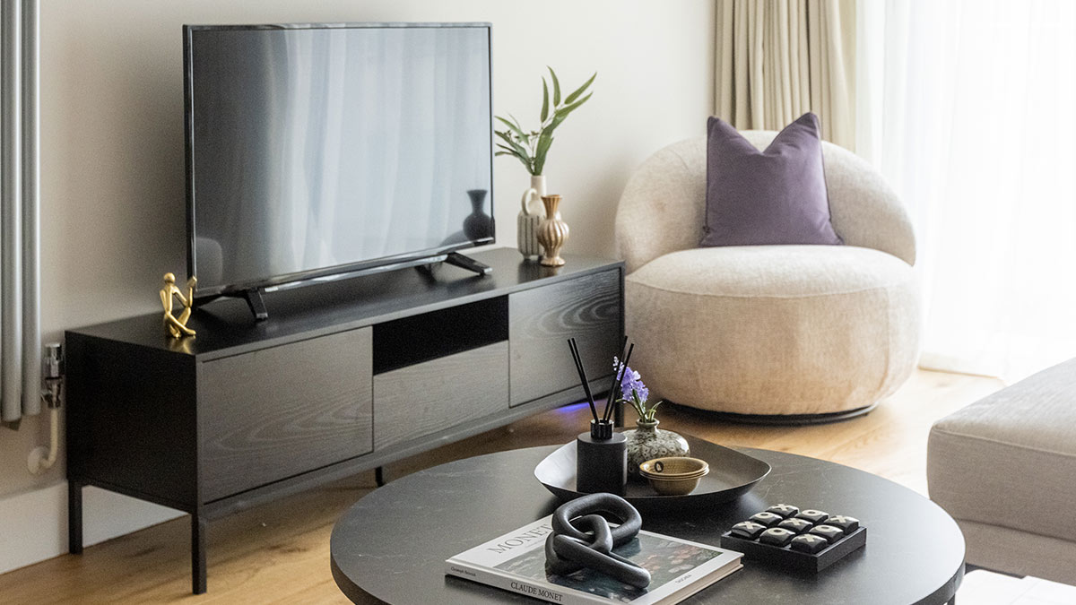 Modern living room with black TV unit, beige accent chair and purple cushion