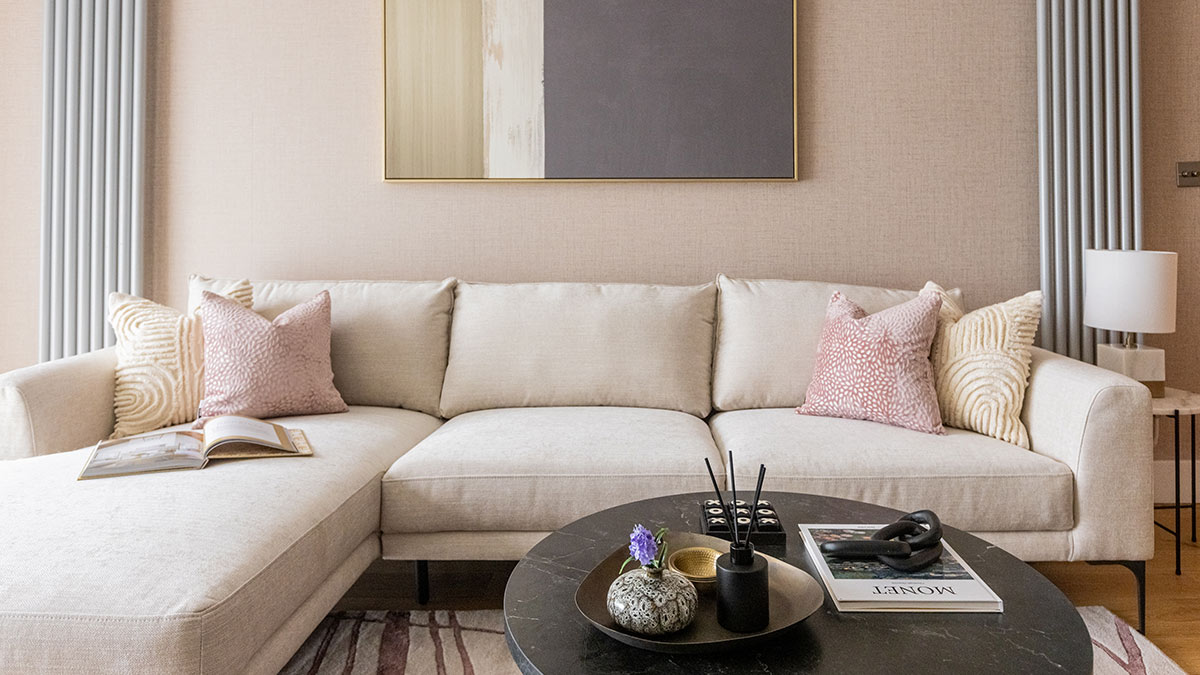 Modern neutral living room with a cream sectional sofa, pink and ivory accent pillows, round black coffee table, and contemporary wall art.