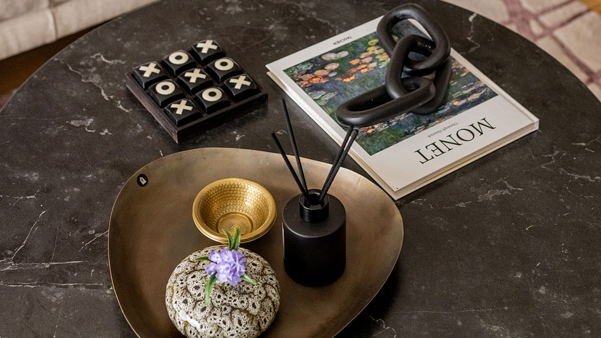 Black marble coffee table styled with a tic-tac-toe board, brass tray, decorative bowl, black reed diffuser, floral vase, and fashion magazine.