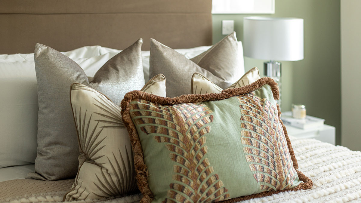 Sage green decorative pillows layered on a luxury bedroom bed with neutral linen cushions