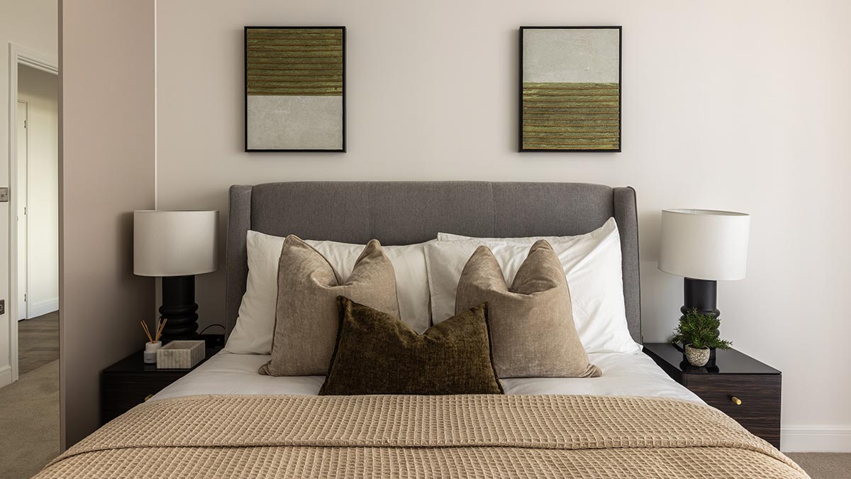 Contemporary bedroom featuring a grey upholstered bed, layered beige cushions, textured throw and matching bedside lamps.