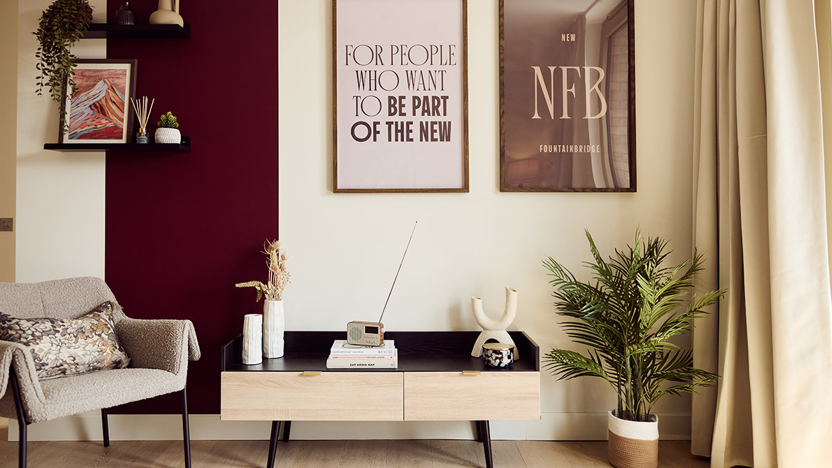 Modern living room with a burgundy accent wall, upholstered armchair, wooden console table, framed artwork and indoor plant