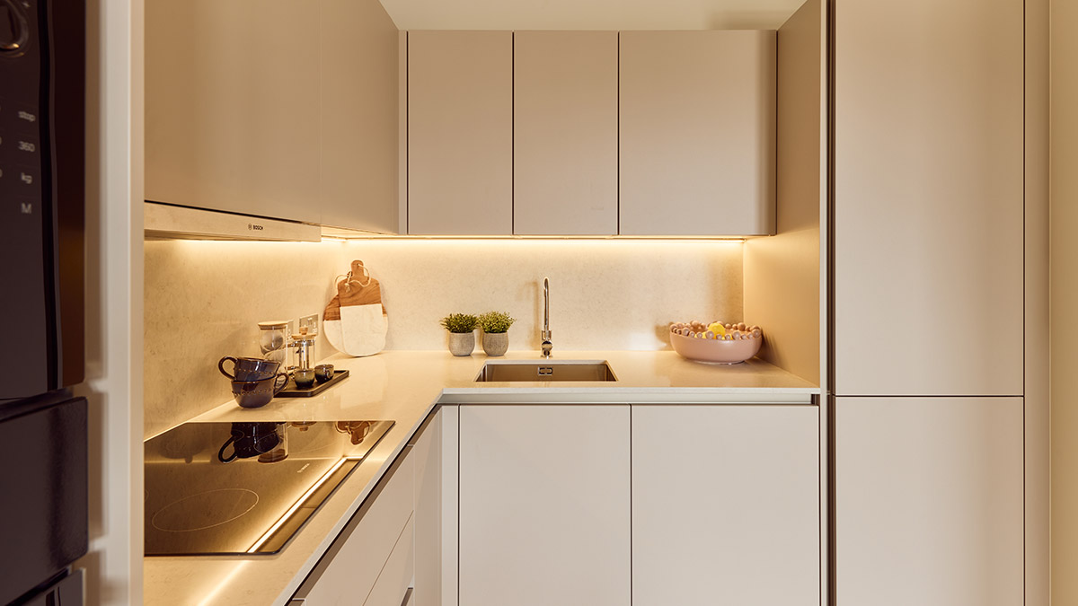 Modern fitted kitchen with beige cabinetry, marble-effect worktops, integrated appliances and warm under-cabinet lighting